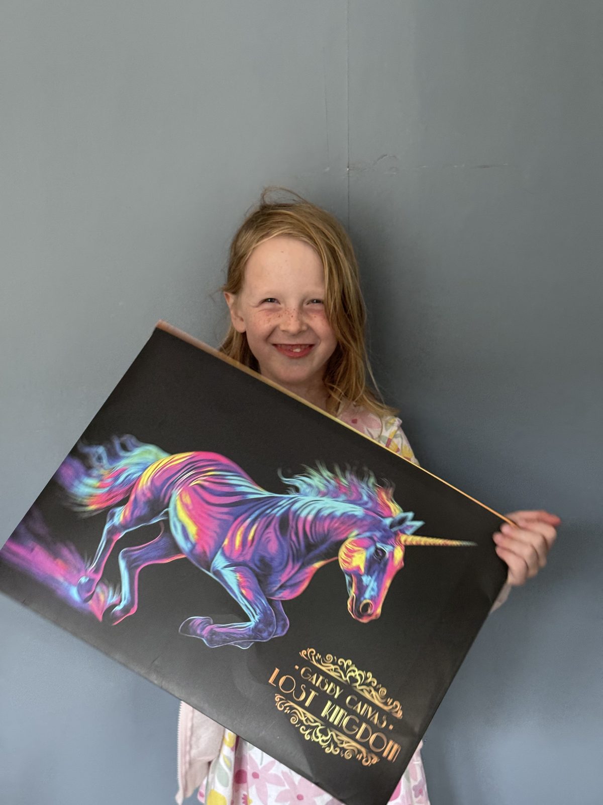 Child smiling behind a unicorn Lost Kingdom canvas